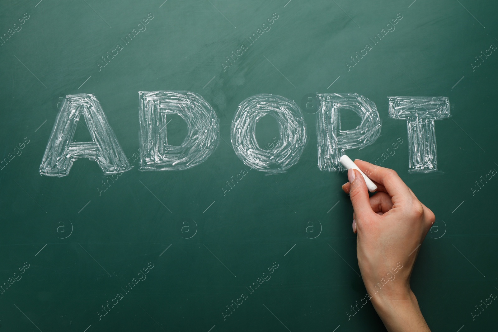 Photo of Woman with chalk writing word Adopt on board, closeup