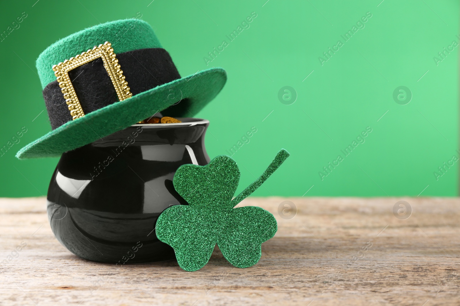 Photo of St. Patrick's day. Pot of gold with leprechaun hat and decorative clover leaf on wooden table. Space for text