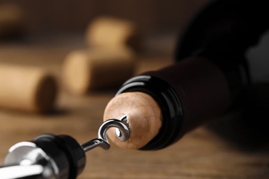 Photo of Opening wine bottle with corkscrew on wooden table, closeup