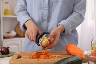 Photo of Woman peeling fresh potato at table indoors, closeup