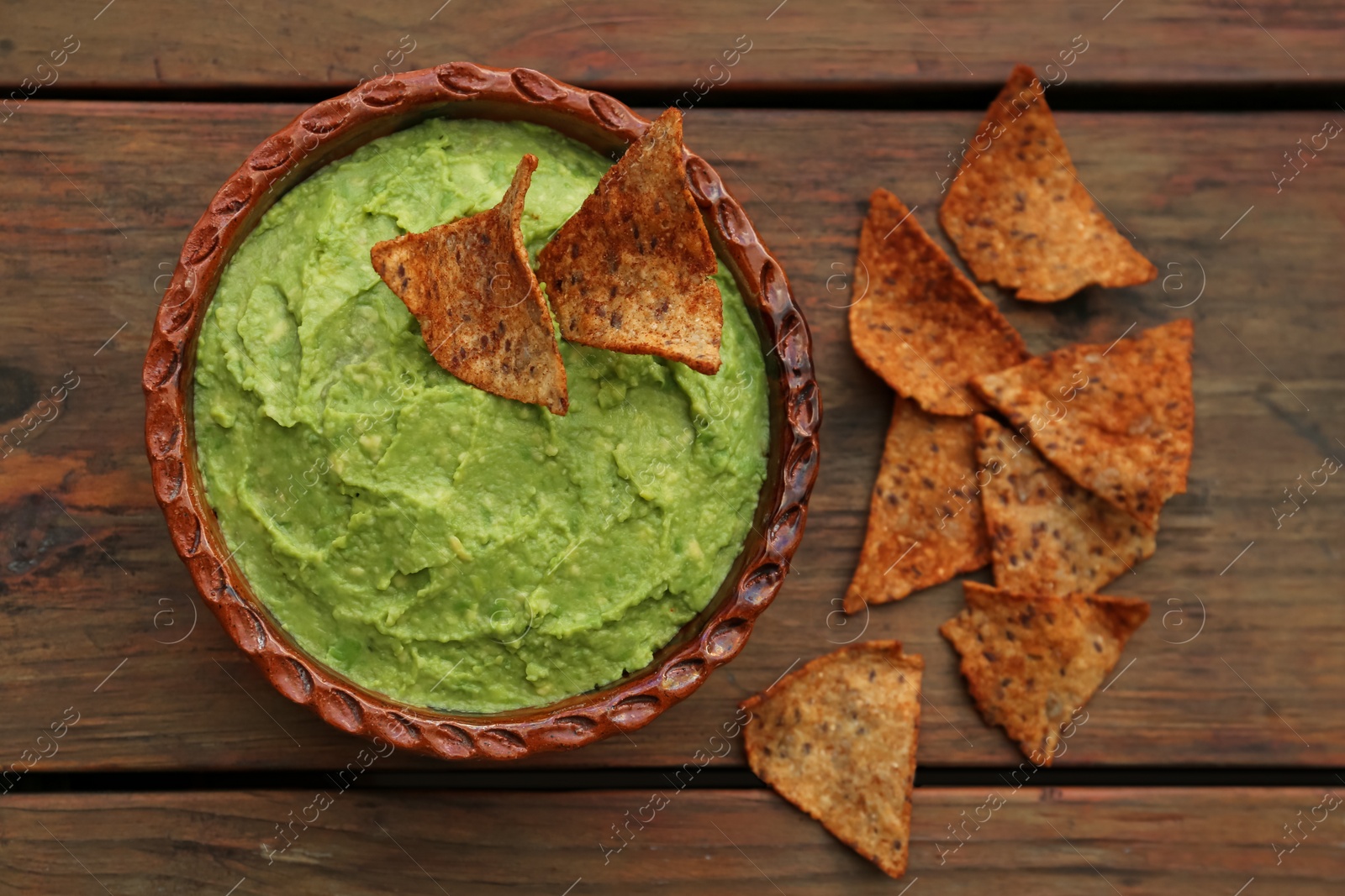 Photo of Delicious guacamole made of avocados and nachos on wooden table, flat lay