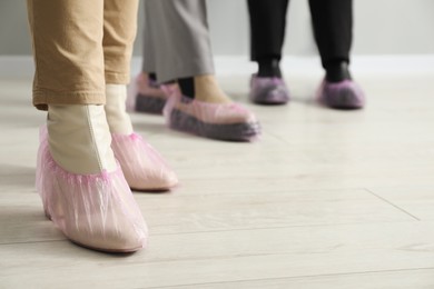 Women wearing pink shoe covers onto different footwear indoors, selective focus