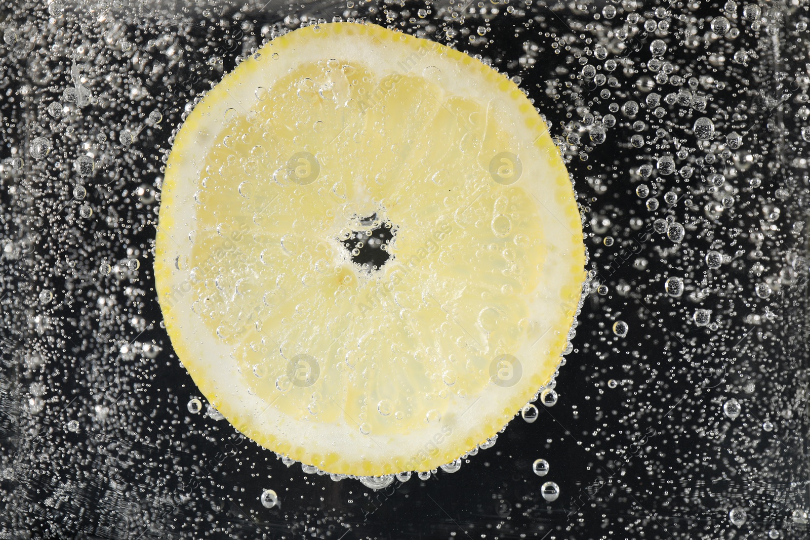 Photo of Juicy lemon slice in soda water against black background, closeup