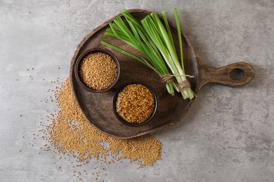 Photo of Serving board with delicious whole grain mustard, seeds and fresh green onion on grey table, top view