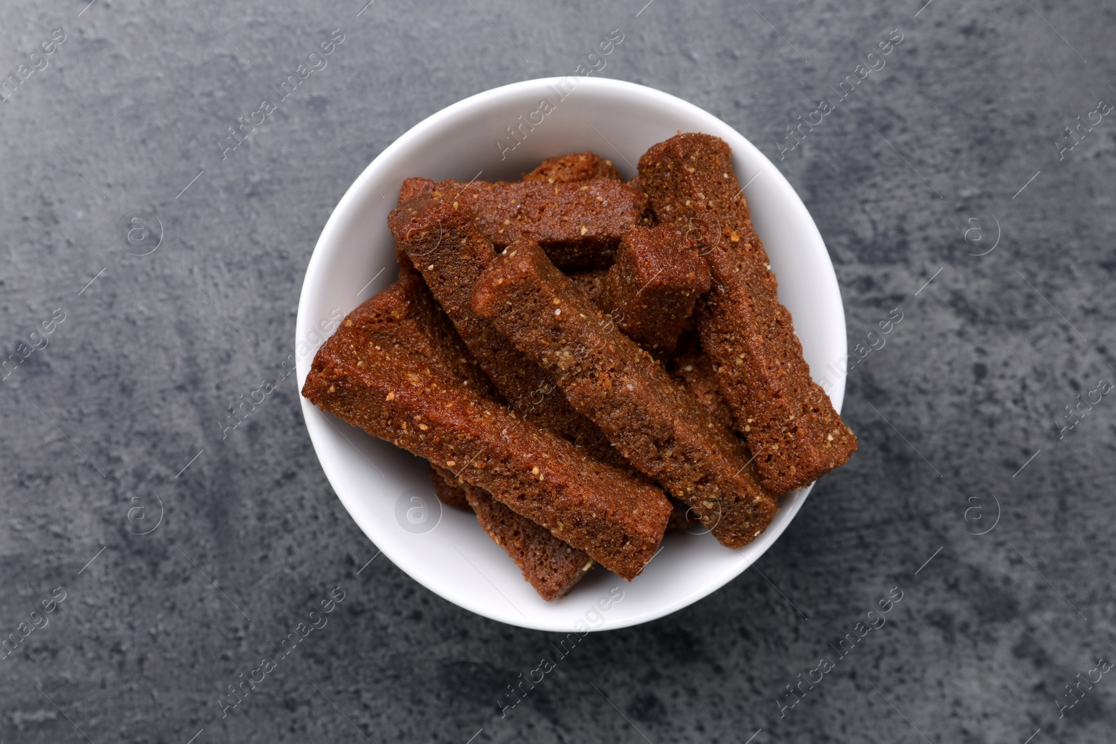 Photo of Crispy rusks in bowl on grey table, top view