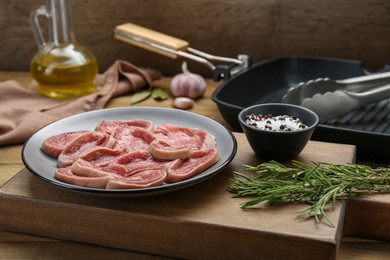 Photo of Raw beef tongue pieces, spices and rosemary on wooden table