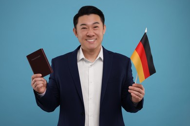 Photo of Immigration. Happy man with passport and flag of Germany on light blue background