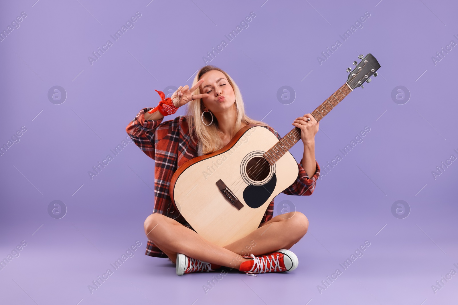 Photo of Hippie woman with guitar showing peace sign on purple background