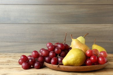 Fresh ripe pears and grapes on wooden table, space for text