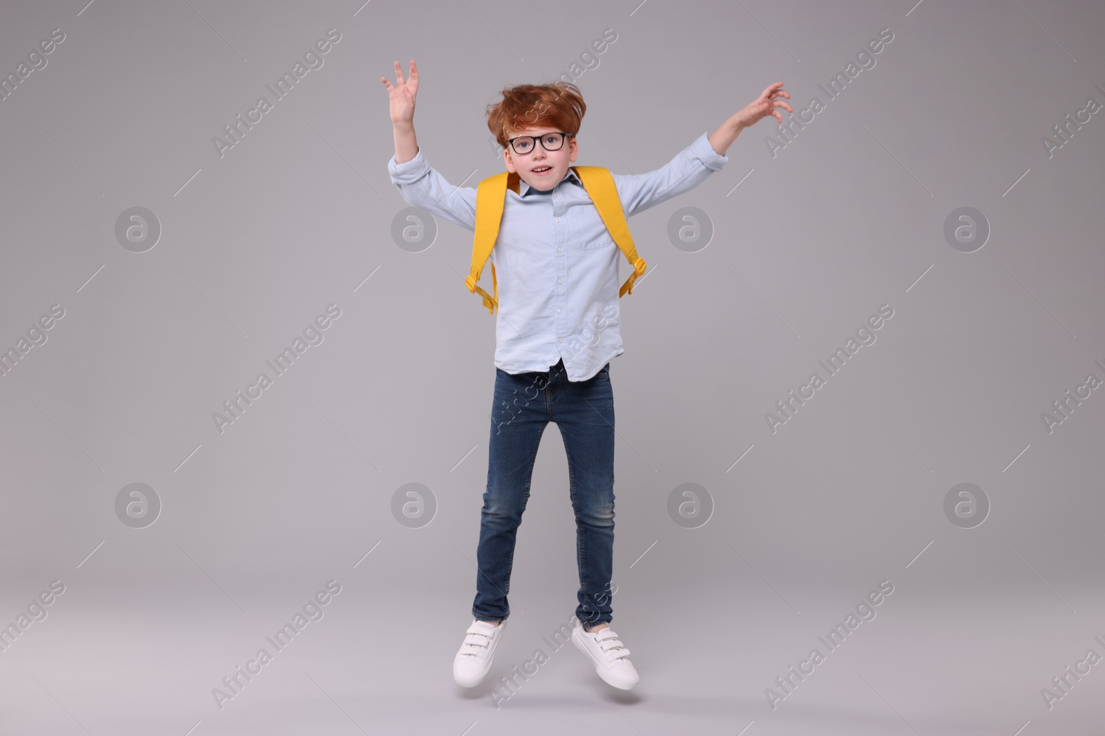 Photo of Happy schoolboy with backpack jumping on grey background