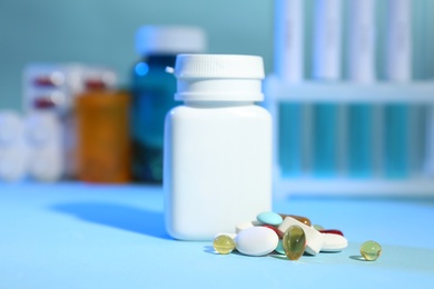 Many different pills near bottle on light blue table
