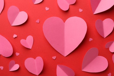 Photo of Pink paper hearts on red background, flat lay