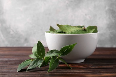 Fresh green bay leaves in bowl on wooden table, closeup