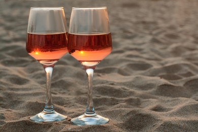 Photo of Glasses of tasty rose wine on sand, space for text