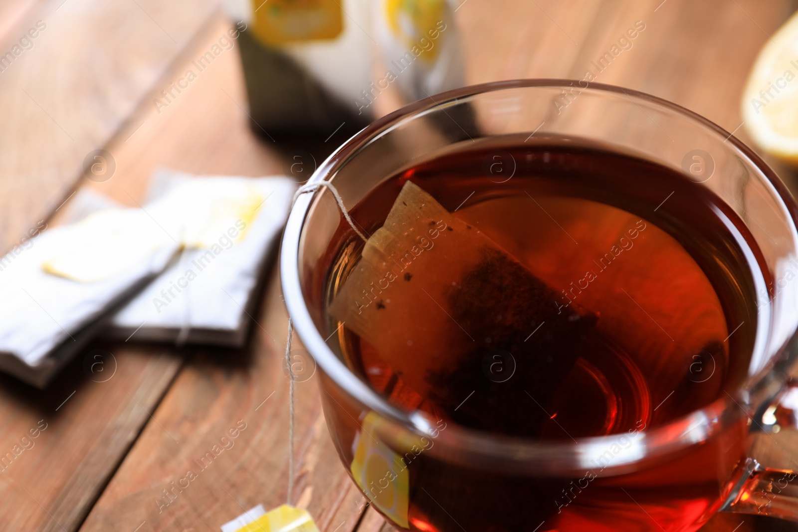 Photo of Tea bag in glass cup on wooden table, closeup