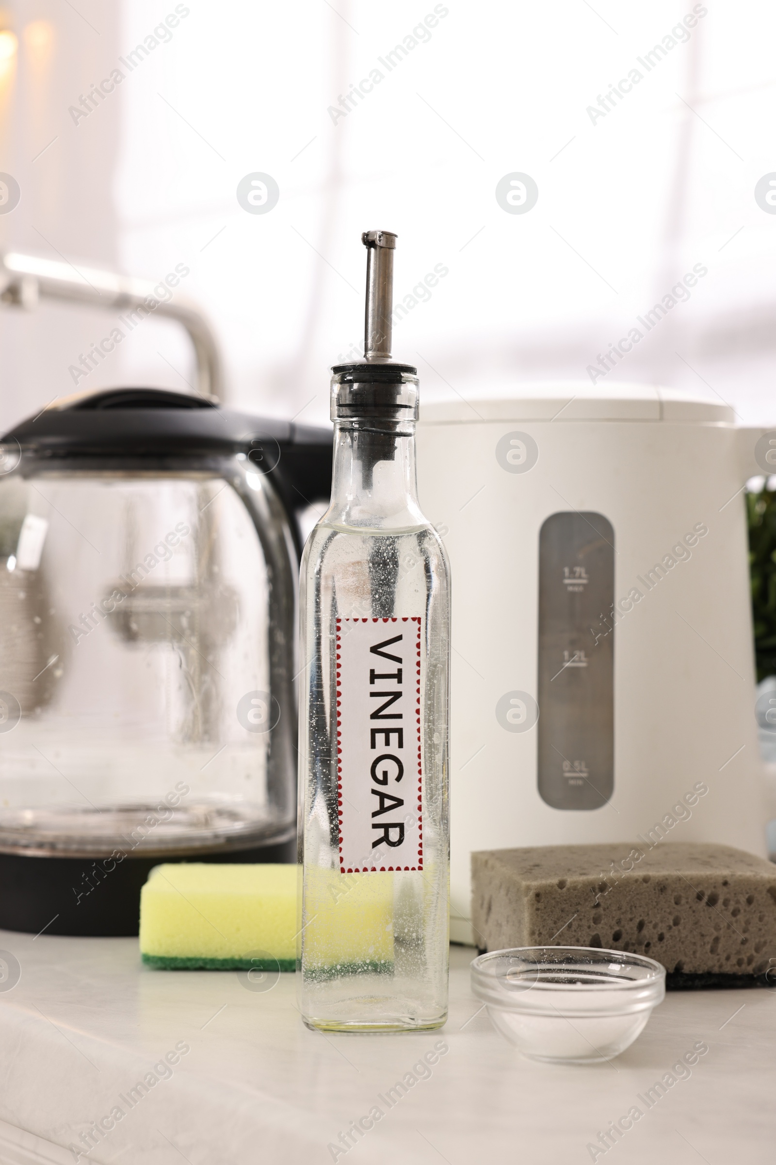 Photo of Cleaning electric kettle. Bottle of vinegar, sponges and baking soda on countertop in kitchen