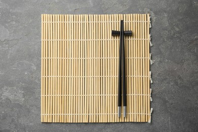 Bamboo mat with pair of black chopsticks and rest on grey table, top view