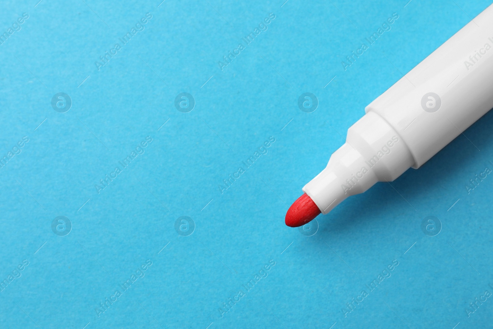 Photo of Bright red marker on light blue background, closeup. Space for text