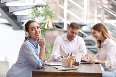 Photo of Young businesswoman with headphones, laptop and her colleagues at table in office