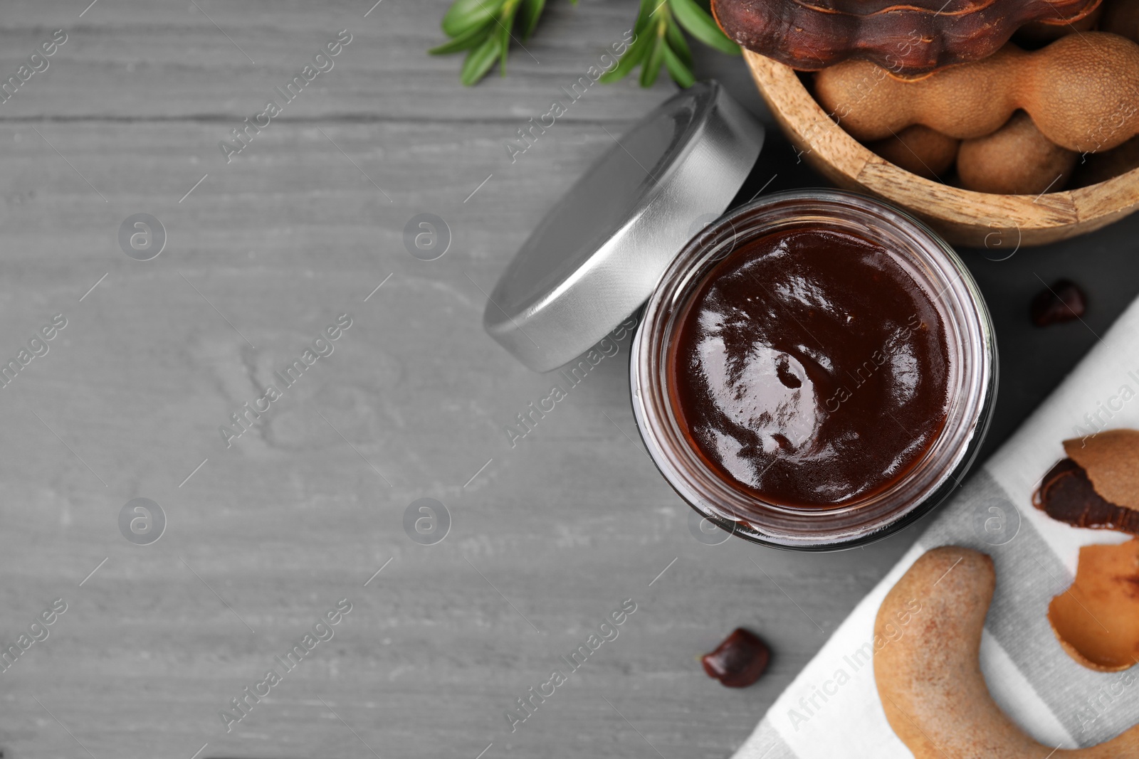 Jar of tasty tamarind sauce and fresh pods on grey wooden table, flat lay. Space for text Photo of Jar of tasty tamarind sauce and fresh pods on grey wooden table, flat lay. Space for text
