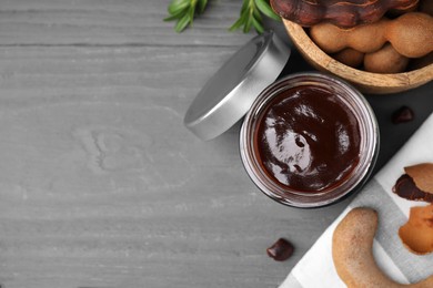 Photo of Jar of tasty tamarind sauce and fresh pods on grey wooden table, flat lay. Space for text