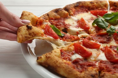 Woman taking piece of delicious Margherita pizza at white table, closeup