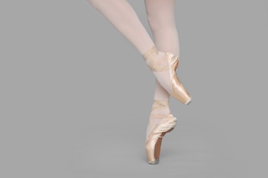 Photo of Young ballerina in pointe shoes practicing dance moves on grey background, closeup