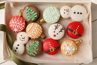 Photo of Beautifully decorated Christmas macarons with ribbon in box on white table, top view