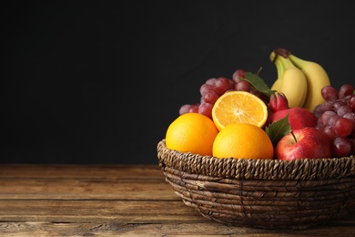 Wicker basket with different fruits on wooden table. Space for text