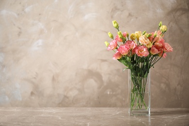 Photo of Eustoma flowers in vase on table near beige wall, space for text