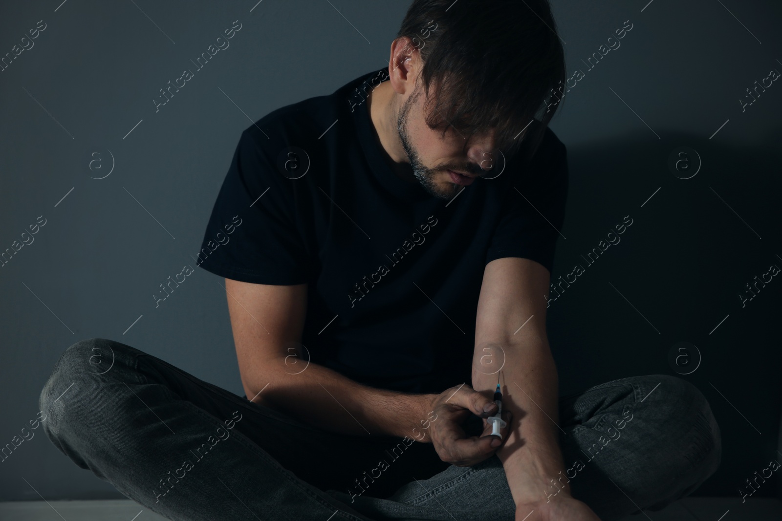 Photo of Male drug addict making injection against grey wall