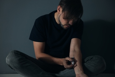 Male drug addict making injection against grey wall