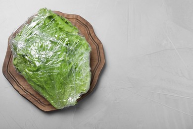Photo of Fresh lettuce in plastic food wrap on light grey table, top view. Space for text