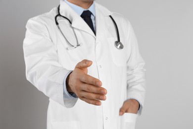 Photo of Male doctor offering handshake on light grey background, closeup