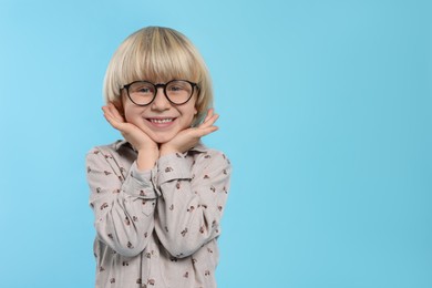 Cute little boy wearing glasses on light blue background, space for text