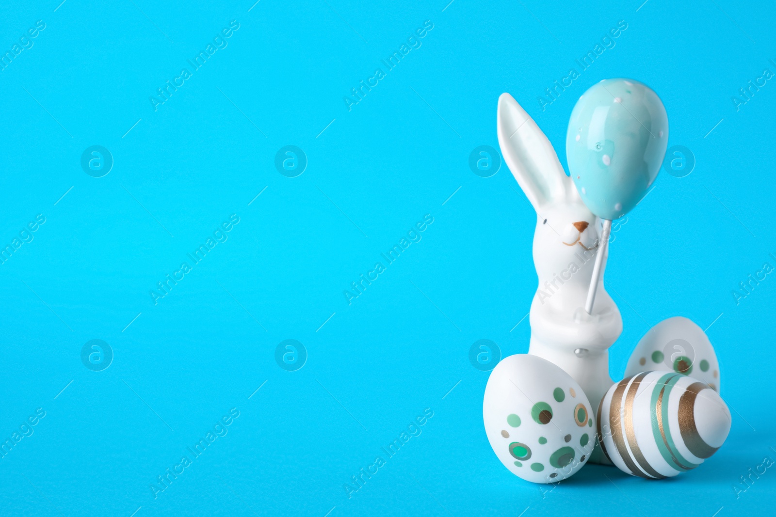 Photo of Easter bunny figure and eggs on blue background. Space for text