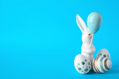 Photo of Easter bunny figure and eggs on blue background. Space for text