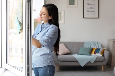 Photo of Young woman cleaning window glass at home