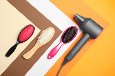 Hair dryer and different brushes on color background, flat lay. Professional hairdresser tool