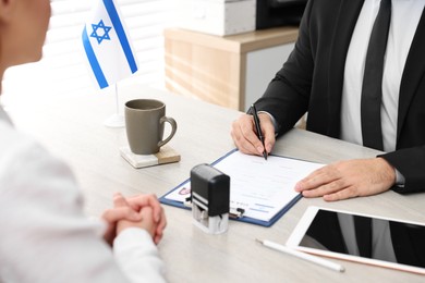 Photo of Immigration to Israel. Embassy worker signing application form at wooden table, closeup