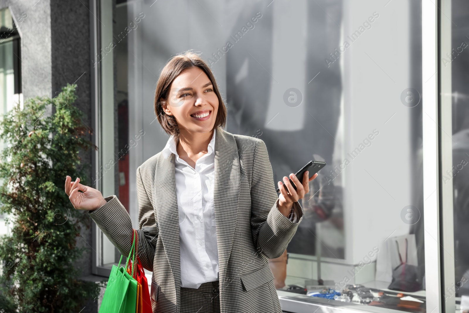 Photo of Special Promotion. Happy young woman with shopping bags and smartphone on city street