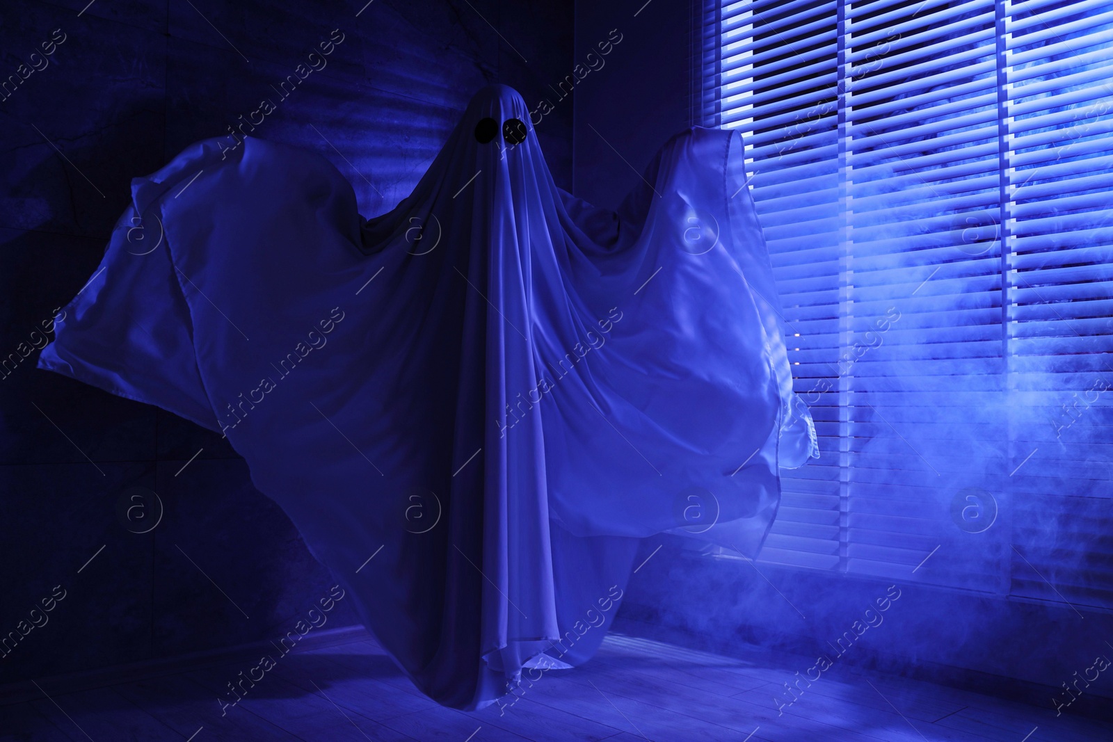 Photo of Creepy ghost. Woman covered with sheet near window in blue light