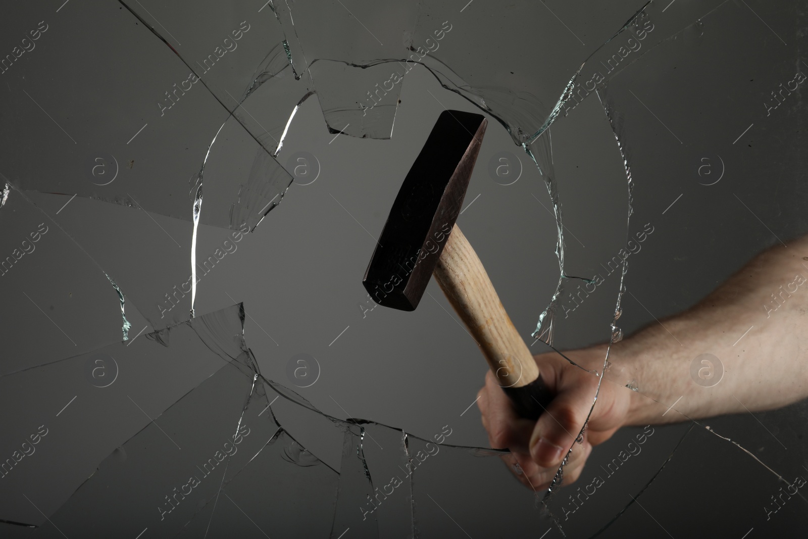 Photo of Man breaking window with hammer on grey background, closeup