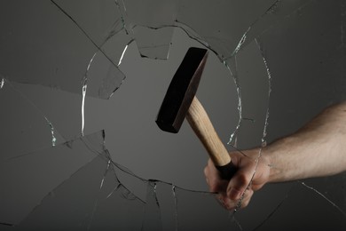Photo of Man breaking window with hammer on grey background, closeup