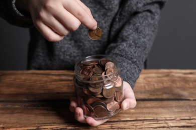 Photo of Woman putting coin into donation jar at wooden table, closeup
