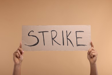 Man holding cardboard banner with word Strike on beige background, closeup