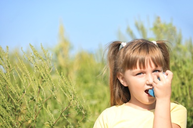 Little girl with inhaler suffering from ragweed allergy outdoors