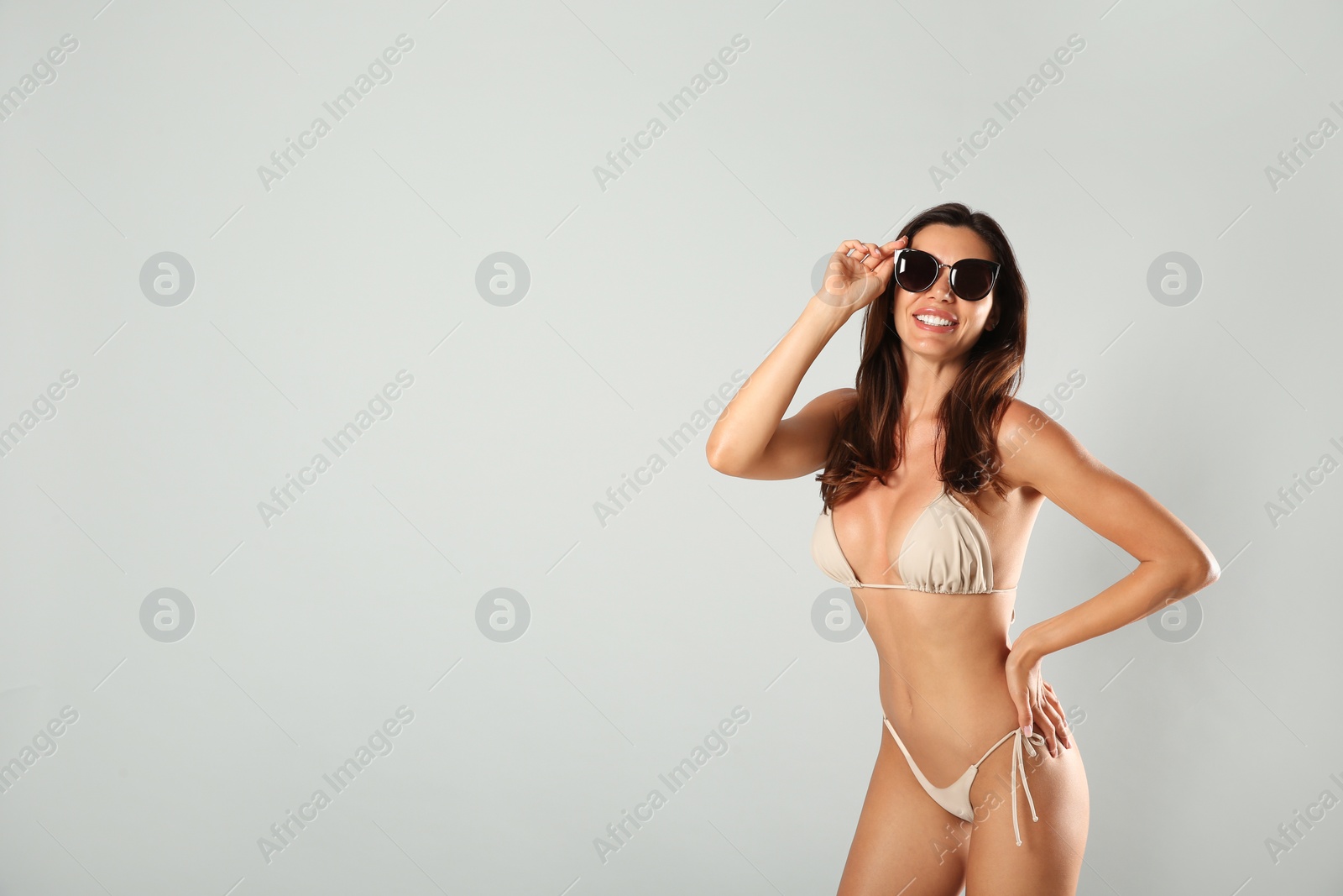 Photo of Beautiful woman in stylish bikini and sunglasses on light grey background. Space for text