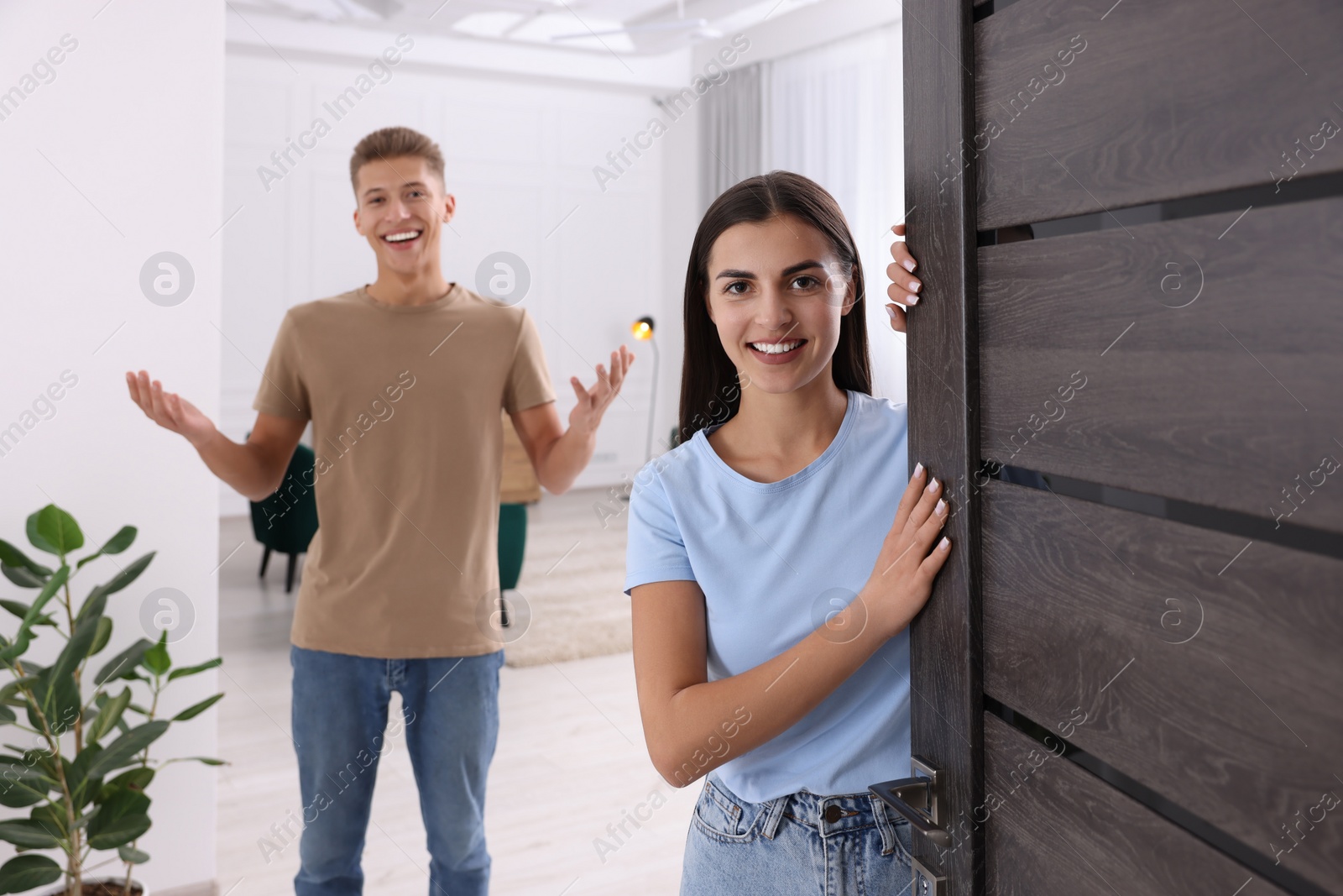 Photo of Happy couple welcoming at home. Invitation to come indoors