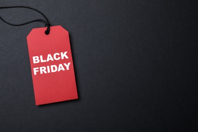 Photo of Red tag with words Black Friday on dark background, top view. Space for text